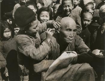 Barber’s assistant cleans ears
after shaving, Tsin Young Koon by 
																	Carl Mydans